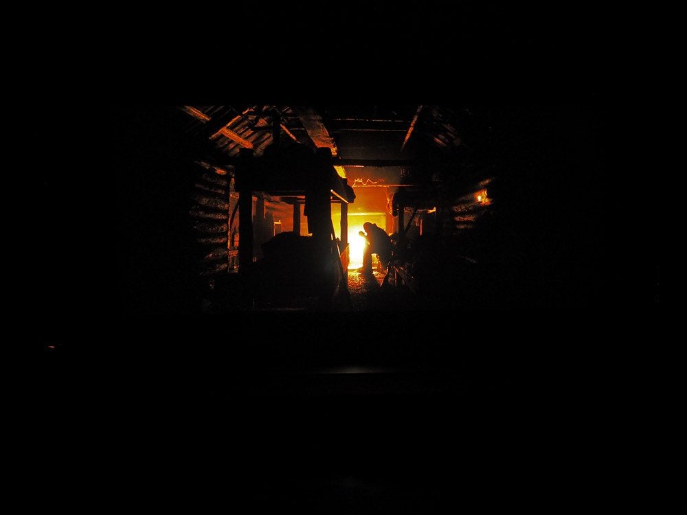 noc, mężczyzna siedzi przy ognisku w drewnianej chacie