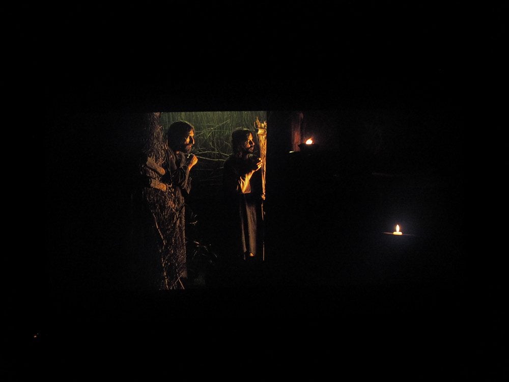 dwie osoby rozmawiają w ciemności, dookoła płomienie świec