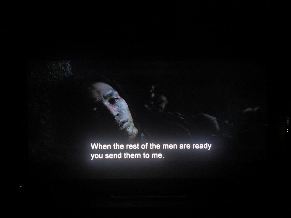 twarz mężczyzny w ciemności, pod spodem długi napis rozjaśnia część ekranu