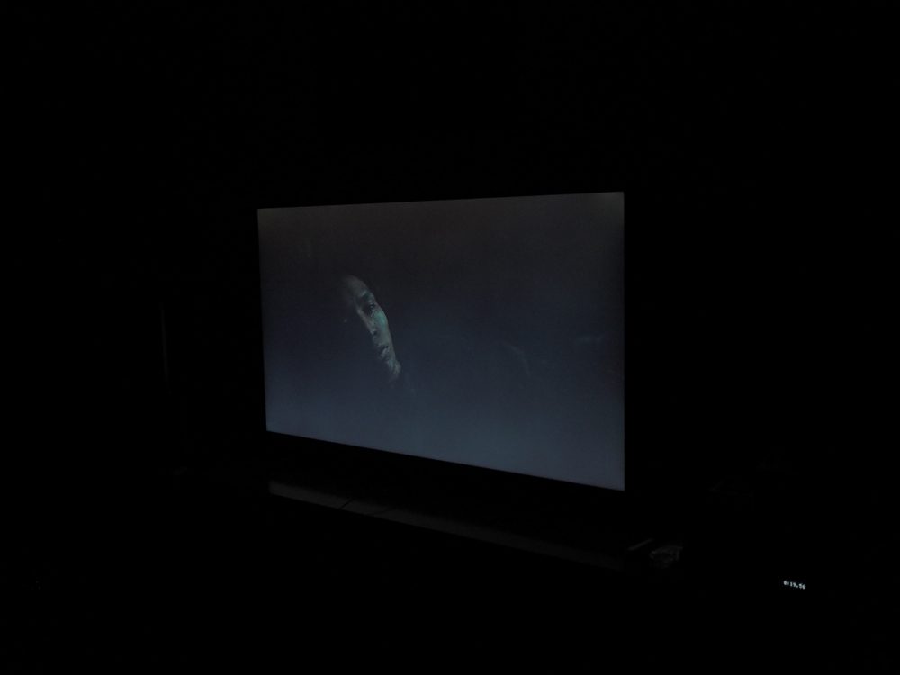 twarz mężczyzny wyłania się z ciemności, czerń ekranu przechodzi w szarość, scena widziana pod kątem