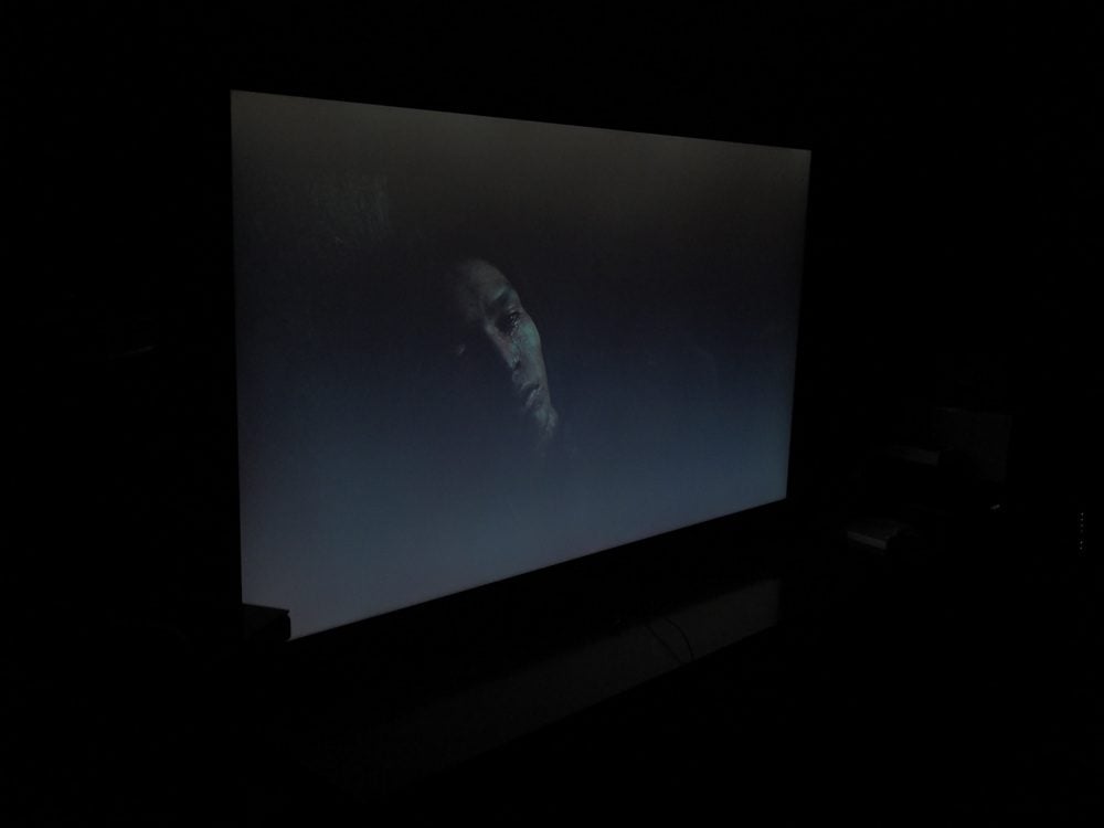 twarz mężczyzny wyłania się z ciemności, czerń ekranu przechodzi w szarość, scena widziana pod kątem