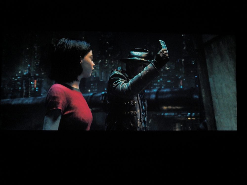 kobieta w czerwonej sukni, obok niej stoi postać w ciemnym stroju, która wyciąga rękę do góry
