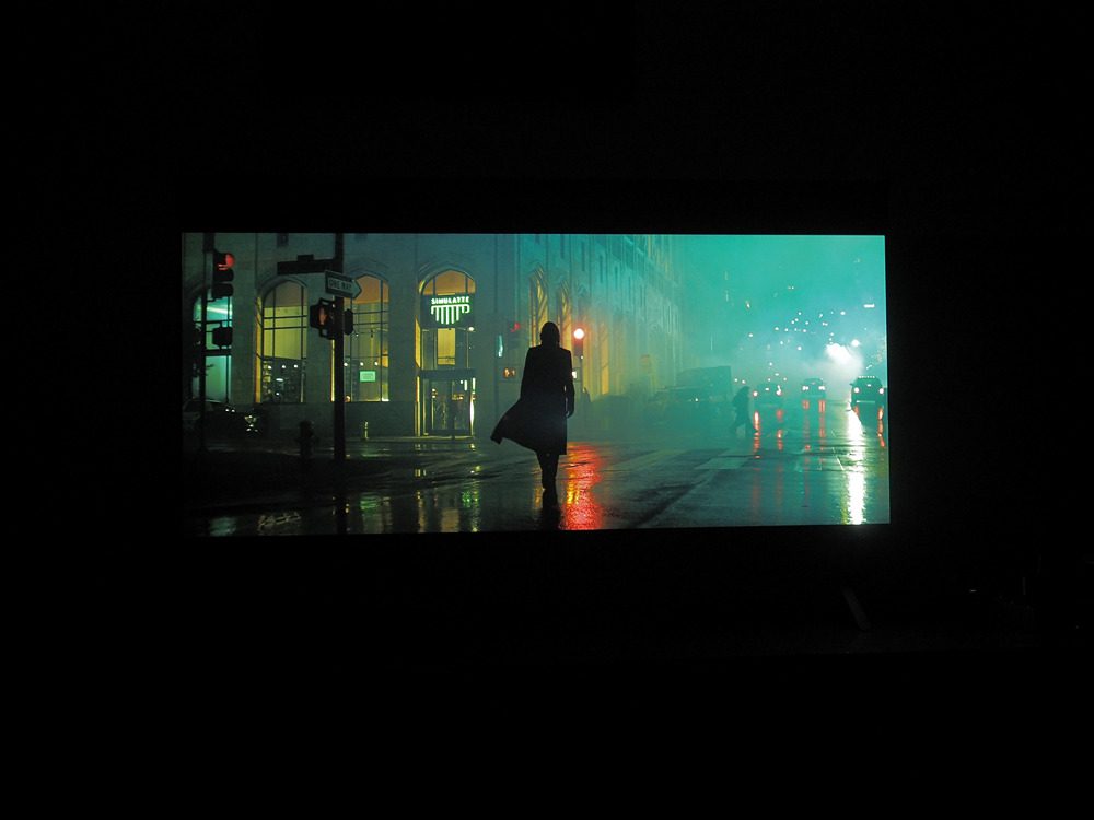 ciemna postać na środku ekranu, dookoła deszczowe miasto
