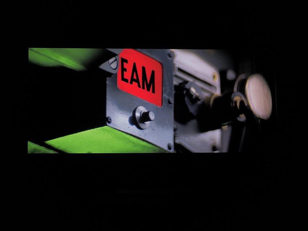 czerwona plakietka z napisem EAM na stalowej płytce, zielone tło